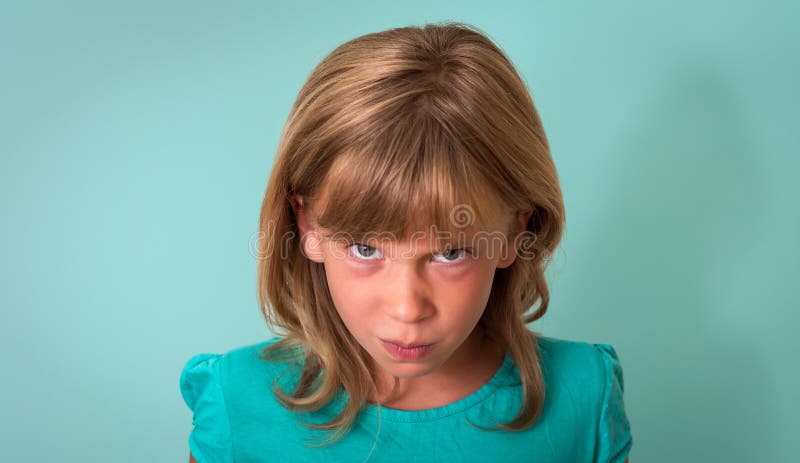 Angry child portrait. Young girl with angry or upset expression on face on turquoise background. Negative human emotion facial expression.