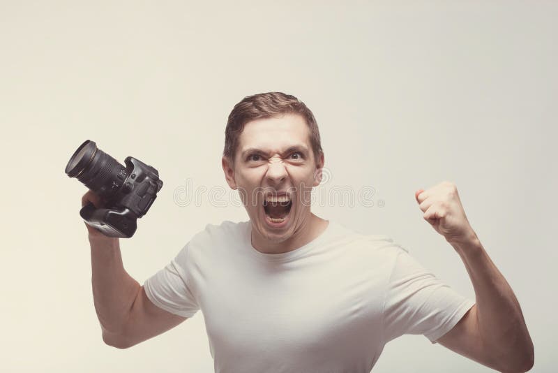 Angry emotional Man with camera isolated on light background. Young man holding digital camera and screaming. Lifestyle, travel royalty free stock photo Angry emotional Man with camera isolated on light background. Young man holding digital camera and screaming. Lifestyle, travel royalty free stock photo