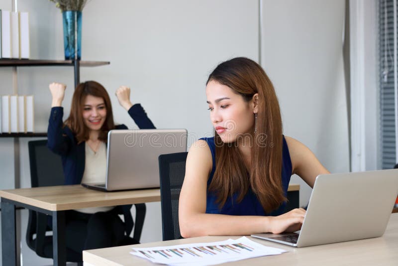 Angry envious Asian business woman looking successful competitor colleague in office.