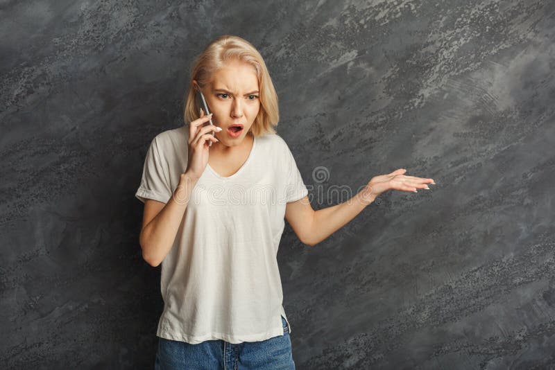 Angry girl arguing by mobile at black studio background