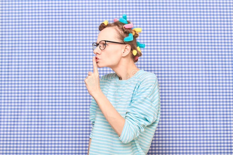 Angry girl with hair curlers on head is showing silence gesture