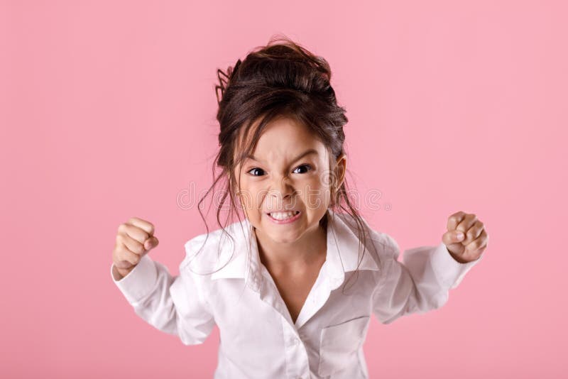 Angry screaming little child girl in white shirt mad raising fist frustrated and furious. on pink background. Human emotions and facial expression. Angry screaming little child girl in white shirt mad raising fist frustrated and furious. on pink background. Human emotions and facial expression