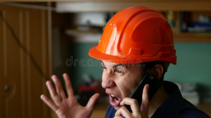 Angry man construction worker in a hardhat shouting, talking on the phone smartphone royalty free stock photo
