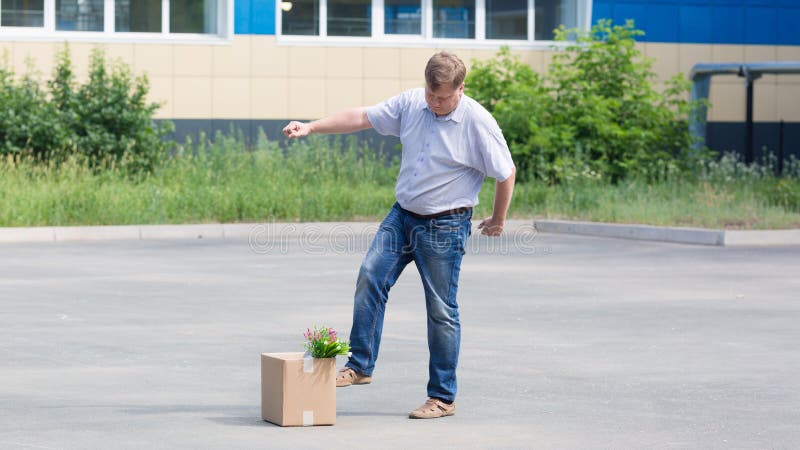 An angry man kicks his box of personal belongings after being fired from work stock photo