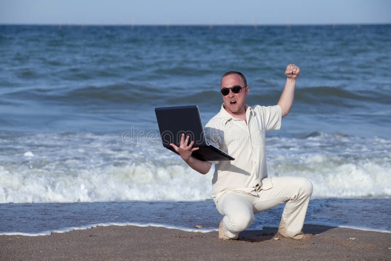 Angry man punching laptop at the beach stock photo