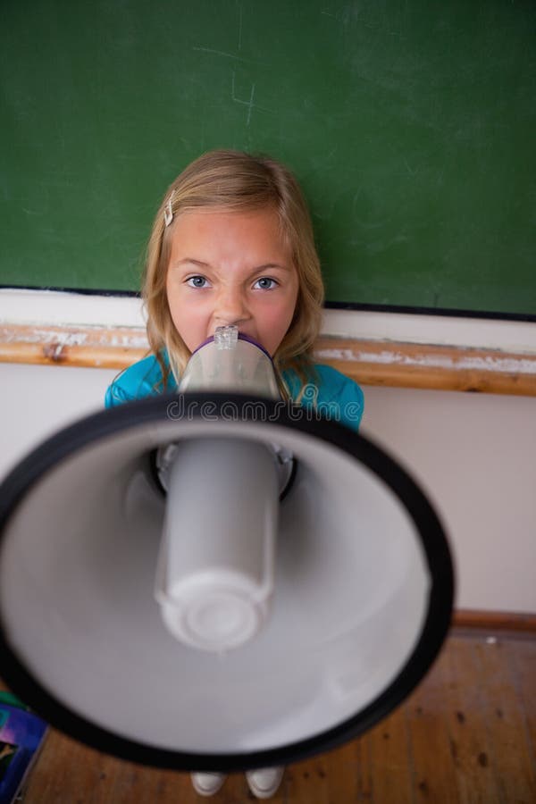 Portrait of an angry schoolgirl yelling through a megaphone in a classroom