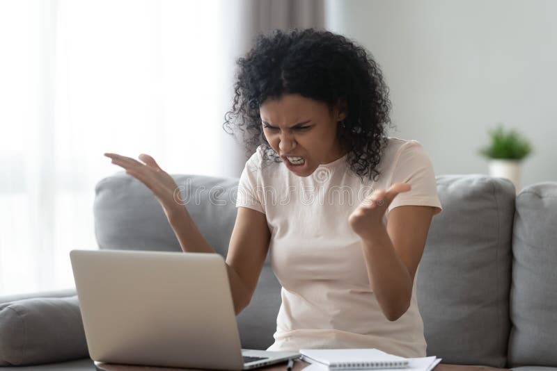 Angry stressed young black woman looking at laptop screen feeling annoyed confused, mad furious african girl in panic frustrated using stuck computer hate problem mistake virus sit on sofa at home. Angry stressed young black woman looking at laptop screen feeling annoyed confused, mad furious african girl in panic frustrated using stuck computer hate problem mistake virus sit on sofa at home