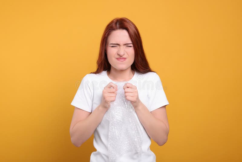 Angry Woman Popping Bubble Wrap on Yellow Background. Stress Relief