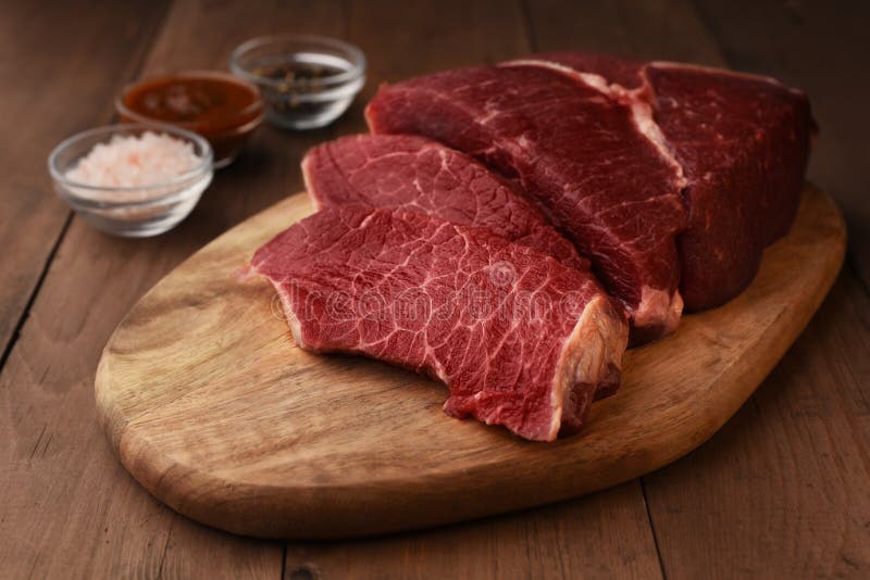 Angus carne de ternera cortada en una tabla de corte de madera. carne roja cruda en un tablero y sazones alrededor de una mesa de madera. salinas y salsa de tomates rojos picantes. listo para cocinar en casa.