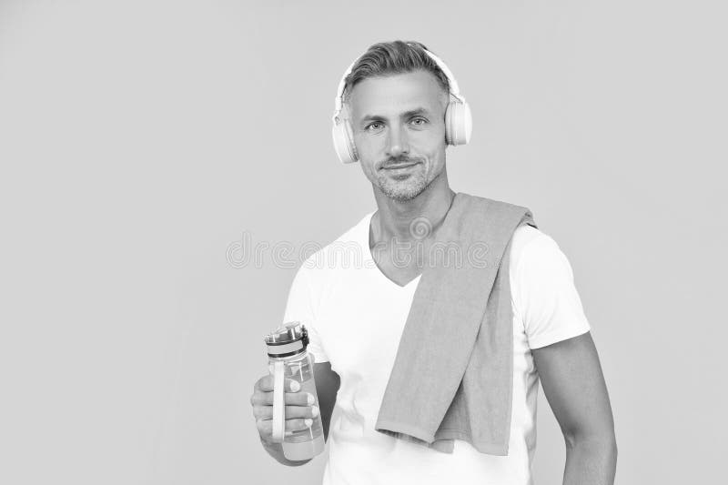 Animado hombre de fitness en auriculares sostiene botella deportiva. hombre de fitness con botella deportiva imagen de archivo libre de regalías