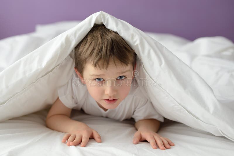 7 anni del ragazzo che si nasconde a letto sotto una coperta o un copriletto bianca immagini stock libere da diritti 7 anni del ragazzo che si nasconde a letto sotto una coperta o un copriletto bianca immagini stock libere da diritti