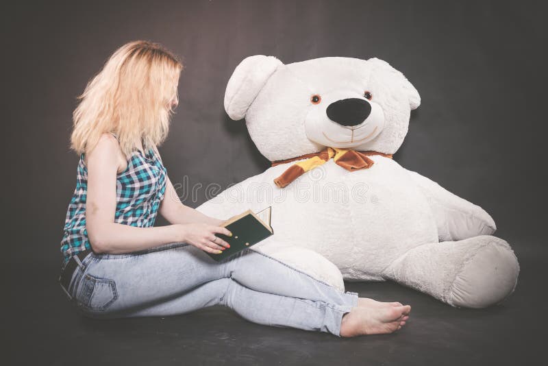 Anni dell'adolescenza biondi svegli nei giochi della camicia di plaid e dei jeans con il suo orso polare dell'orsacchiotto enorme immagine stock libera da diritti Anni dell'adolescenza biondi svegli nei giochi della camicia di plaid e dei jeans con il suo orso polare dell'orsacchiotto enorme immagine stock libera da diritti