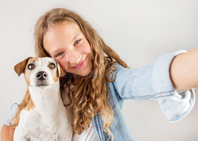 Anni dell'adolescenza sorridenti con il cane che fa la foto del selfie sullo smartphone sopra la ragazza sveglia del fondo bianco fotografia stock Anni dell'adolescenza sorridenti con il cane che fa la foto del selfie sullo smartphone sopra la ragazza sveglia del fondo bianco fotografia stock