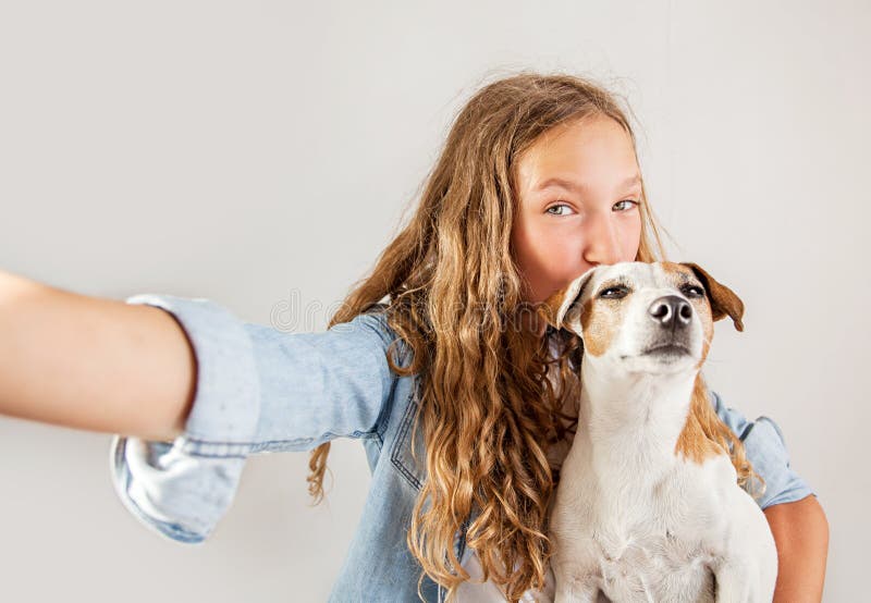 Anni dell'adolescenza sorridenti con il cane che fa la foto del selfie sullo smartphone sopra la ragazza sveglia del fondo bianco fotografia stock libera da diritti Anni dell'adolescenza sorridenti con il cane che fa la foto del selfie sullo smartphone sopra la ragazza sveglia del fondo bianco fotografia stock libera da diritti