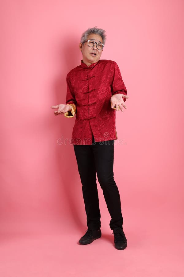 Happy Chinese new year. Asian Chinese energetic senior man wearing red traditional cheongsam qipao or changshan dress with gesture of not a big deal, unbothered, clueless isolated on pink background. Happy Chinese new year. Asian Chinese energetic senior man wearing red traditional cheongsam qipao or changshan dress with gesture of not a big deal, unbothered, clueless isolated on pink background