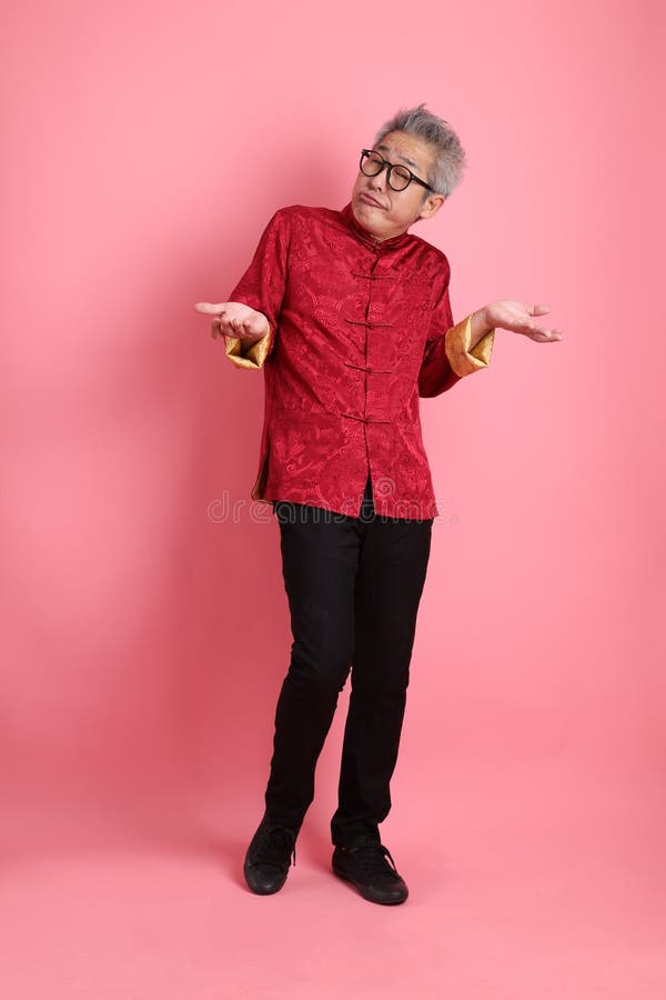 Happy Chinese new year. Asian Chinese energetic senior man wearing red traditional cheongsam qipao or changshan dress with gesture of not a big deal, unbothered, clueless isolated on pink background. Happy Chinese new year. Asian Chinese energetic senior man wearing red traditional cheongsam qipao or changshan dress with gesture of not a big deal, unbothered, clueless isolated on pink background