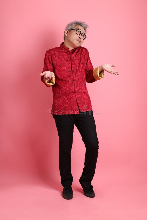 Happy Chinese new year. Asian Chinese energetic senior man wearing red traditional cheongsam qipao or changshan dress with gesture of not a big deal, unbothered, clueless isolated on pink background. Happy Chinese new year. Asian Chinese energetic senior man wearing red traditional cheongsam qipao or changshan dress with gesture of not a big deal, unbothered, clueless isolated on pink background