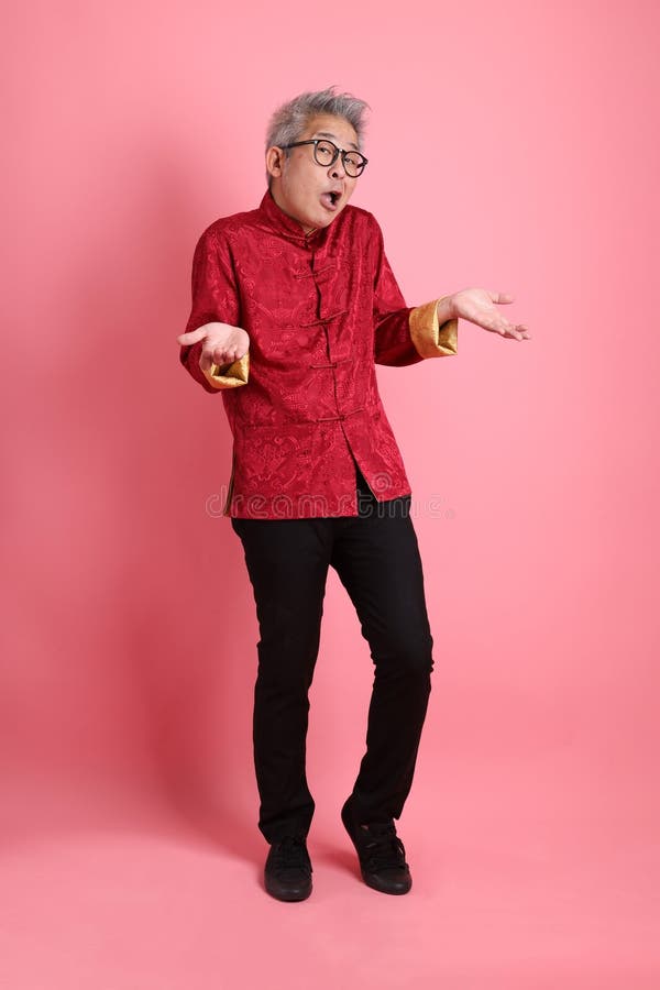 Happy Chinese new year. Asian Chinese energetic senior man wearing red traditional cheongsam qipao or changshan dress with gesture of not a big deal, unbothered, clueless isolated on pink background. Happy Chinese new year. Asian Chinese energetic senior man wearing red traditional cheongsam qipao or changshan dress with gesture of not a big deal, unbothered, clueless isolated on pink background