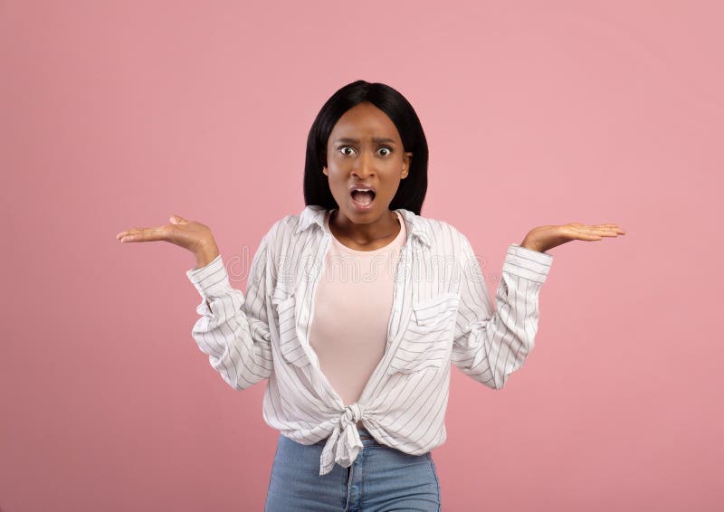 Annoyed African American woman gesturing I DON`T KNOW, shrugging her shoulders on pink studio background. Puzzled black lady cannot understand something, unsure about making choice
