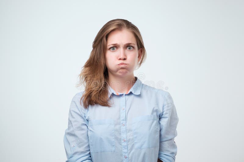 Annoyed irritated young female in blue shirt blowing her cheeks, frowning, feeling frustrated with something.