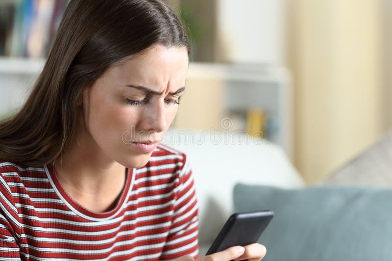 Annoyed woman checking smart phone sitting on a sofa in the living room at home. Annoyed woman checking smart phone sitting on a sofa in the living room at home