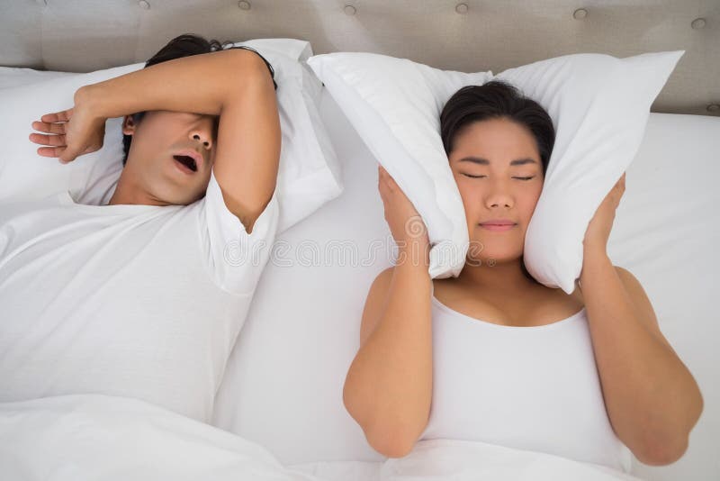 Annoyed woman covering her ears with pillows to block out snoring royalty free stock images Annoyed woman covering her ears with pillows to block out snoring royalty free stock images
