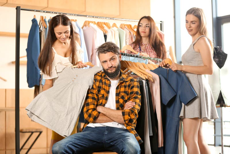 Annoyed young man waiting for his girlfriend and her friends while they choosing clothes in shop royalty free stock photos Annoyed young man waiting for his girlfriend and her friends while they choosing clothes in shop royalty free stock photos
