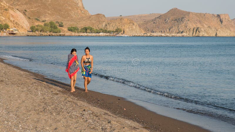 Années de l'adolescence et femme marchant le long de la plage avec des serviettes enroulées autour du Th images stock Années de l'adolescence et femme marchant le long de la plage avec des serviettes enroulées autour du Th images stock
