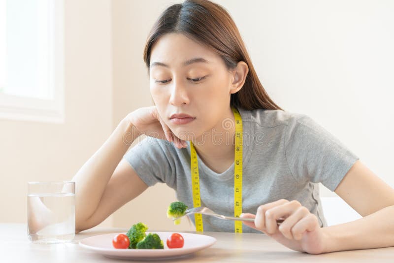 Anoressia infelice ragazza asiatica a dieta che tiene la forchetta nei broccoli nel piatto dell'insalata non gradita o stanca di m