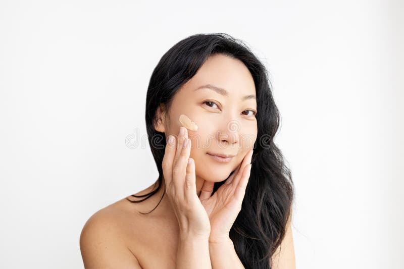 Ansiktsmakeup. Stängning av vackra asiatiska handdukar som lägger grunden på ansiktshuden. arkivbild