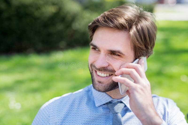 Handsome businessman phone calling on smartphone sitting in the city park. Working remotely, waiting for business meeting. Manager smiling, outdoor in urban setting. Handsome businessman phone calling on smartphone sitting in the city park. Working remotely, waiting for business meeting. Manager smiling, outdoor in urban setting.