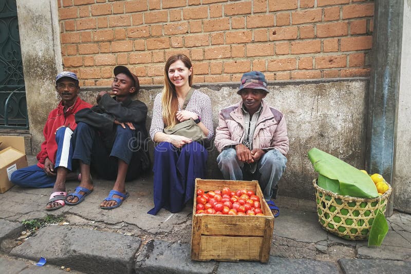 Antananarivo, Madagascar - April 24, 2019: Young caucasian woman sitting with local fruit sellers at Antananarivo high street. royalty free stock photography Antananarivo, Madagascar - April 24, 2019: Young caucasian woman sitting with local fruit sellers at Antananarivo high street. royalty free stock photography