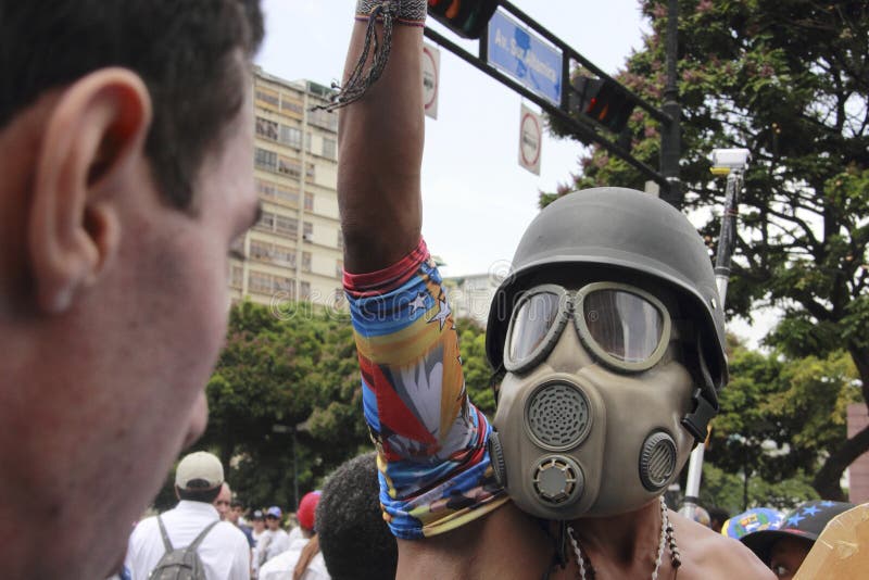 Anti vestir dos protestadores de Nicolas Maduro lança gás lacrimôgeneo a máscara durante as manifestações em massa que transforma fotografia de stock Anti vestir dos protestadores de Nicolas Maduro lança gás lacrimôgeneo a máscara durante as manifestações em massa que transforma fotografia de stock