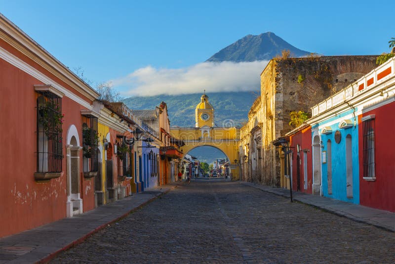 Cityscape of Antigua city at sunrise with its colonial style facades and the colorful yellow Santa Catalina arch and the Agua volcano in the background, Guatemala, Central America. Cityscape of Antigua city at sunrise with its colonial style facades and the colorful yellow Santa Catalina arch and the Agua volcano in the background, Guatemala, Central America.