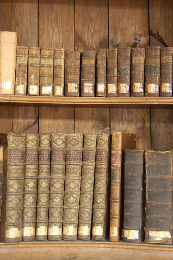 A view of old, antique books on shelves in a wooden bookcase. A view of old, antique books on shelves in a wooden bookcase.