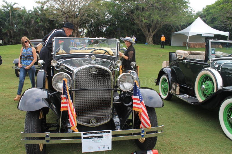 Face and headlamps on antique american car at event. 1931 ford model a roadster parked on grass among other old fords. lady and gentleman in period attire.