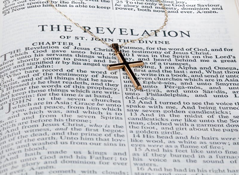 Old fashioned gold cross and chain laying on a page from the bible on the revelation. Old fashioned gold cross and chain laying on a page from the bible on the revelation