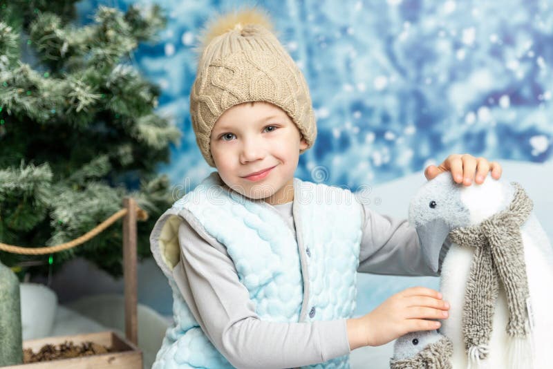 Anul nou și de Crăciun. băiețelul care stă cu pinguini cu jucării moi pe fond decorat pe timp de iarnă stock photo