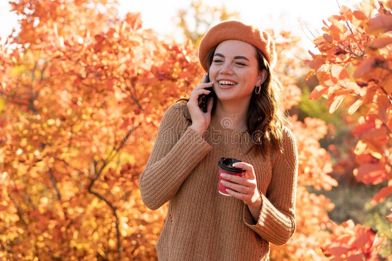 Anvisningar om lyckliga unga kvinnor i höstparken. glad tjej pratar på en smart telefon utomhus i en orange röd arkivfoto