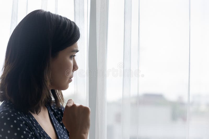 Side view of anxious sad young asian woman crying alone looking at window. Depressed millennial female going through hard bad life times cheating betrayal of beloved man divorce separation. Copy space