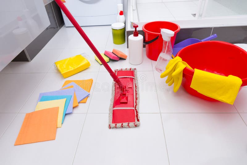 Display of assorted cleaning products on the clean white tiled floor in a bathroom with cloths, sponges, mop, bucket, basin and various chemicals and detergents. Display of assorted cleaning products on the clean white tiled floor in a bathroom with cloths, sponges, mop, bucket, basin and various chemicals and detergents