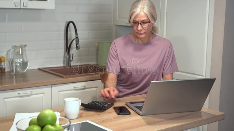 Anziana che scrive su computer portatile e calcolatrice stock footage
