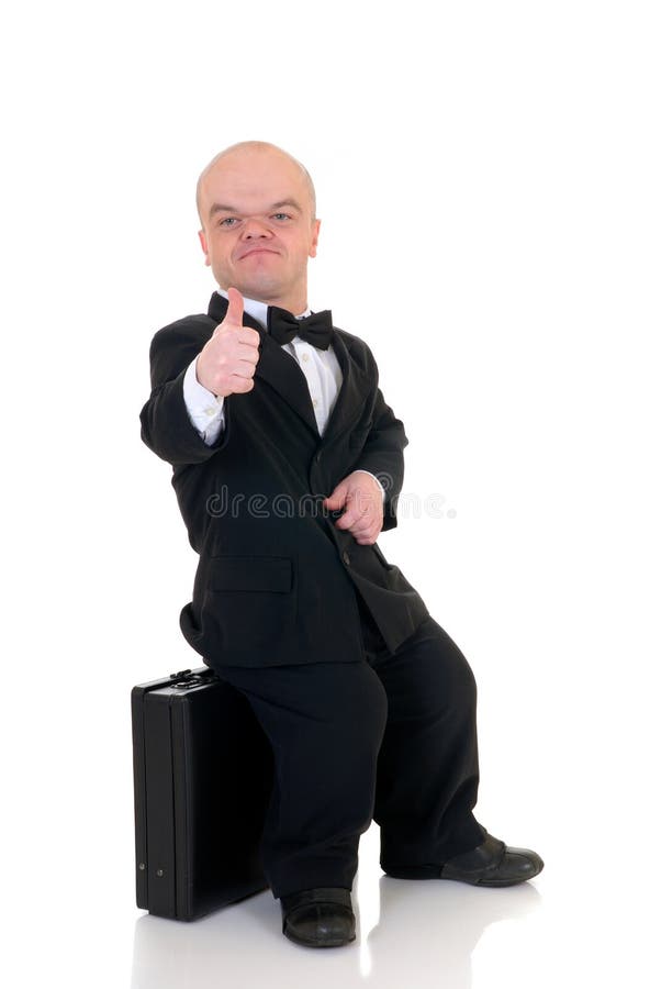 Little businessman, dwarf in a formal suit with bow tie next to suitcase, studio shot, white background. Little businessman, dwarf in a formal suit with bow tie next to suitcase, studio shot, white background