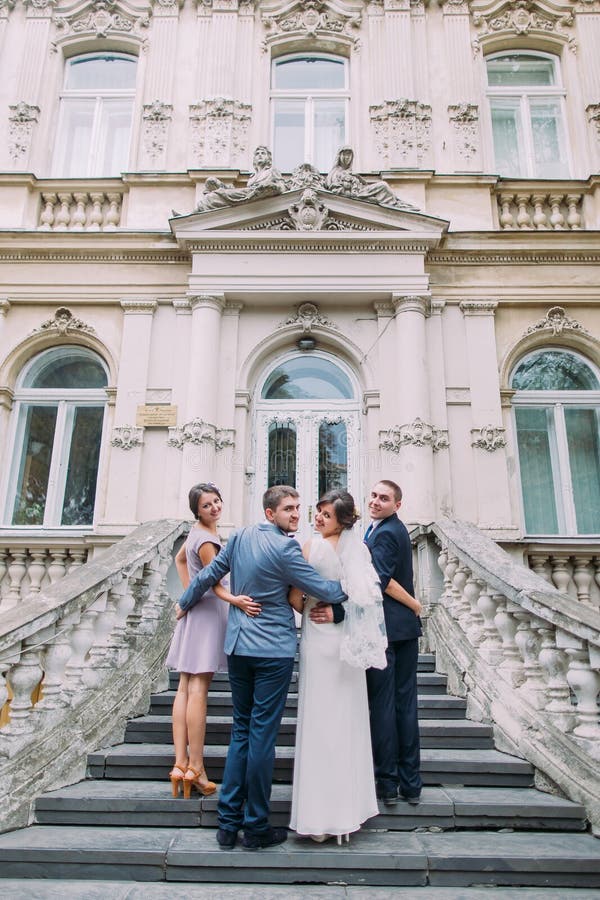 Apenas pareja casada alegre con el padrino de boda feliz y la dama de honor que presentan en las escaleras del edificio clásico fotografía de archivo libre de regalías Apenas pareja casada alegre con el padrino de boda feliz y la dama de honor que presentan en las escaleras del edificio clásico fotografía de archivo libre de regalías