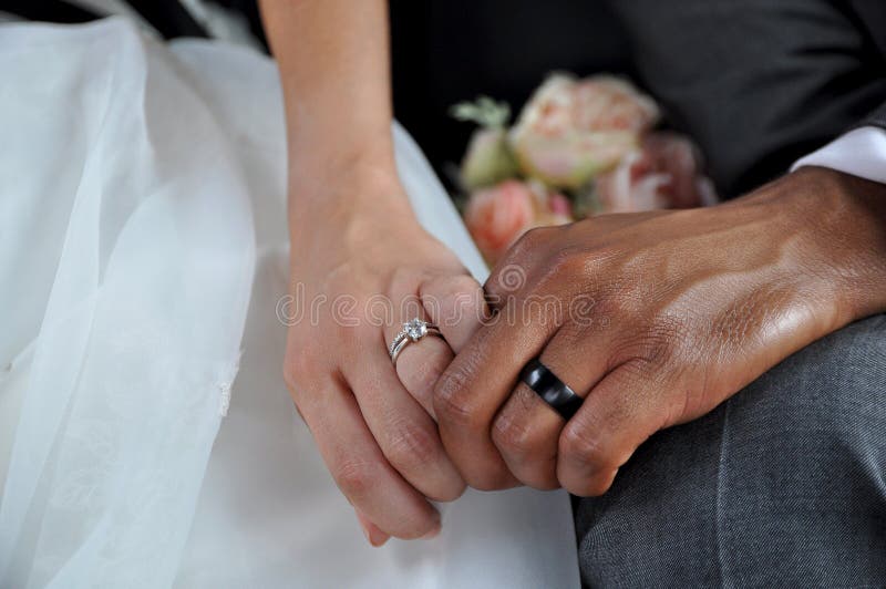 Apenas pares inter-raciais casados que guardam as mãos que vestem as alianças de casamento imagens de stock Apenas pares inter-raciais casados que guardam as mãos que vestem as alianças de casamento imagens de stock