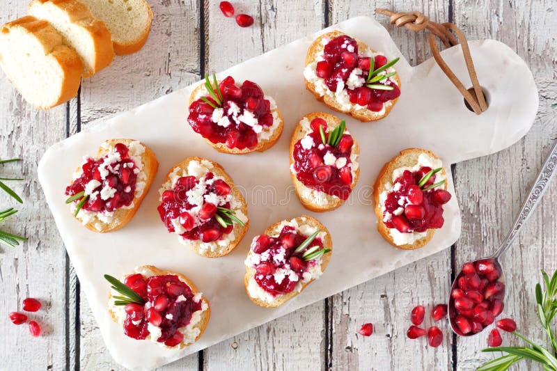 Aperitivi di crostini di festa con i mirtilli rossi, i melograni e la feta, vista superiore su un vassoio bianco immagini stock Aperitivi di crostini di festa con i mirtilli rossi, i melograni e la feta, vista superiore su un vassoio bianco immagini stock