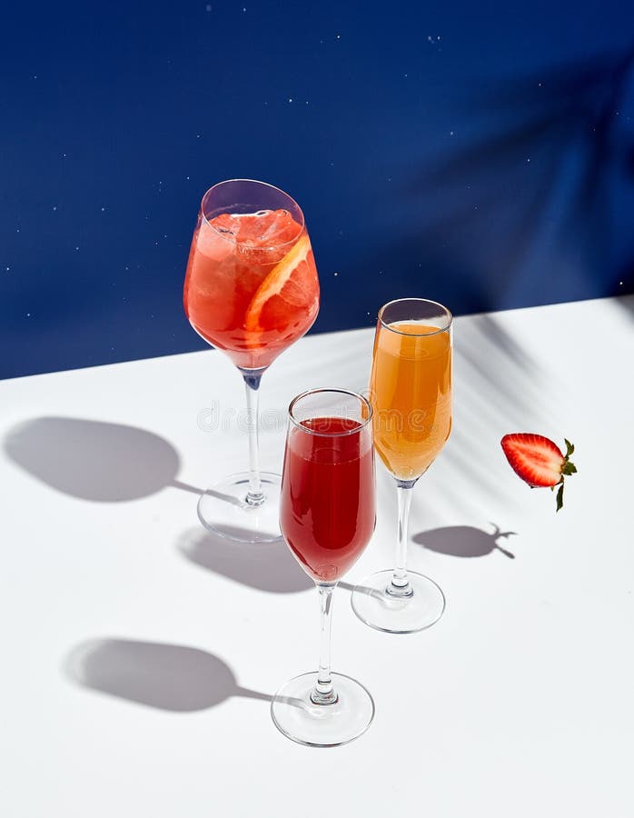 Aperol drink and bellini cocktail on white table with blue background. Sunshine and palm leaf shadow drink modern still life.