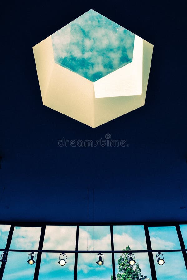 A vertical shot of a hexagonal opening on the ceiling of a building with lights and glass walls underneath. A vertical shot of a hexagonal opening on the ceiling of a building with lights and glass walls underneath