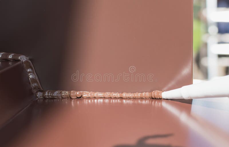 Applying a brown silicone sealant to a metal joint. Applying a brown silicone sealant to a metal joint