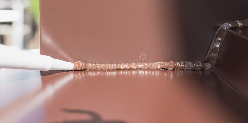 Applying a brown silicone sealant to a metal joint. Applying a brown silicone sealant to a metal joint